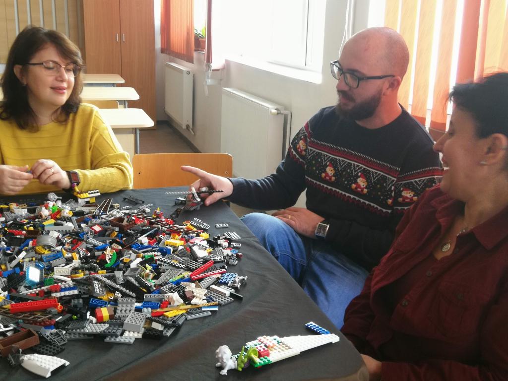 Profesori discutând în jurul unei mese acoperite cu piese LEGO, la un atelier SuperDascăl.